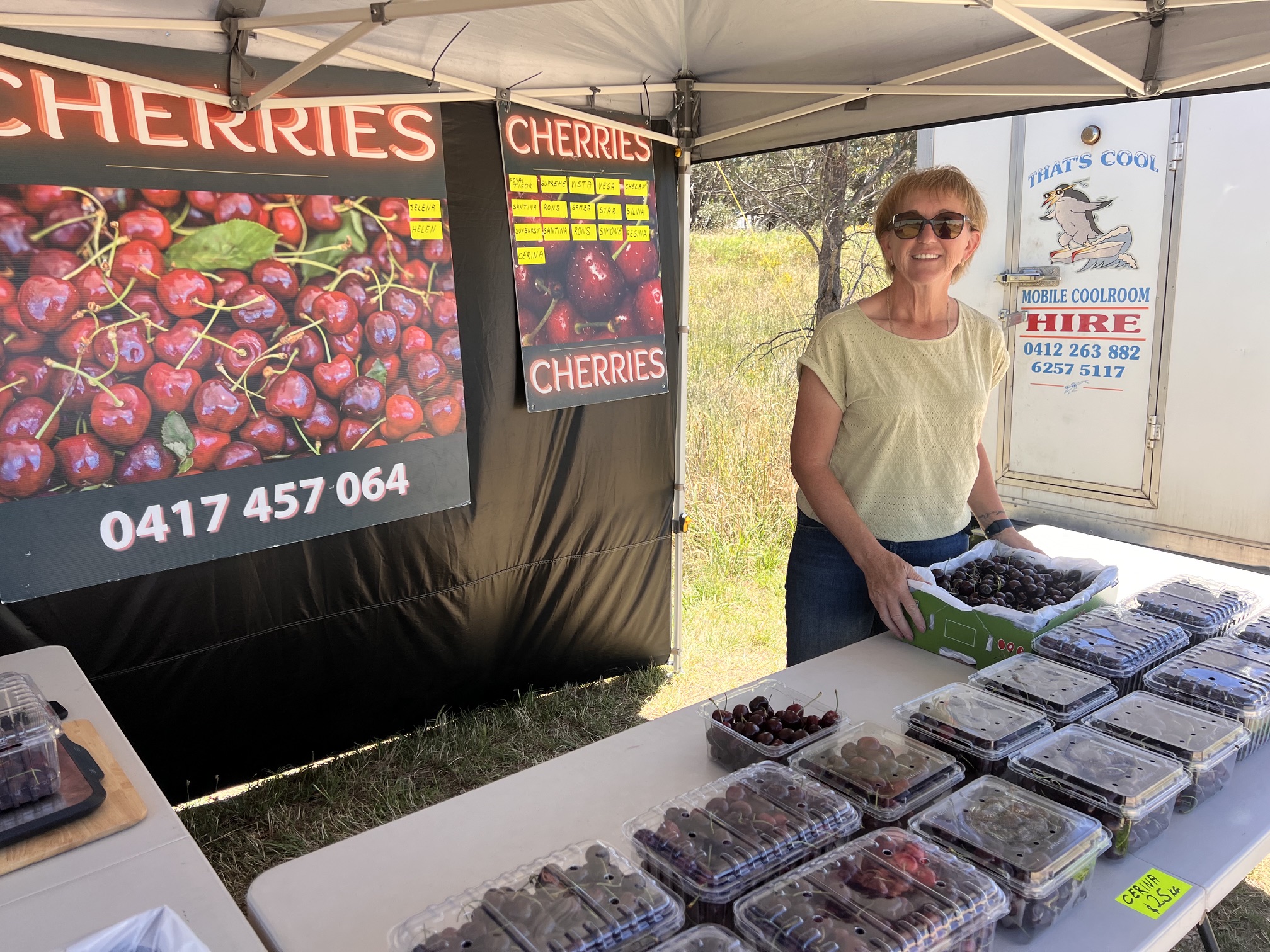 Cerina Cherries owner smiling with a box of fresh cherries at the market stall